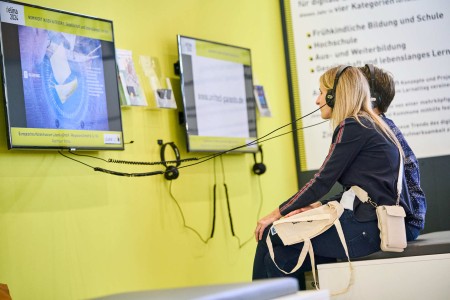 Zwei Frauen betrachten die Videos der Nominierten und Gewinner am delina-Stand. 